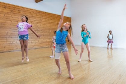A group of girls stretch and jump in a dance studio
