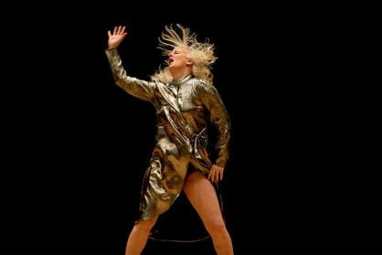 An older woman in a metallic dress head bangs so her hair flies into the air