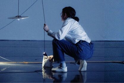 A person crouches in a space around hanging ropes and lights