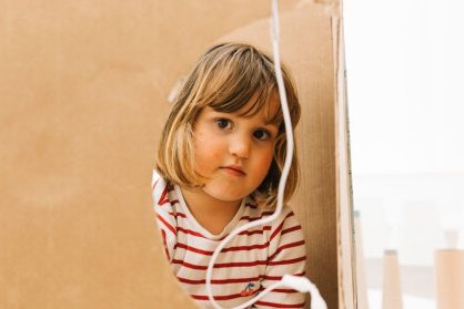A young person peeps through a hole in a box