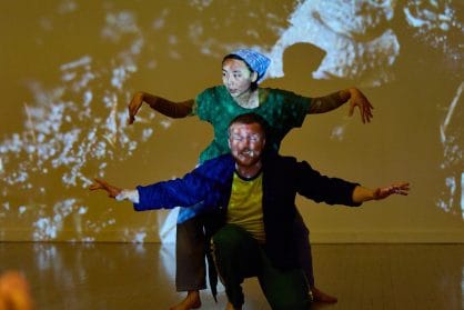 2 dancers are positioned crouching with their arms bent out like wings. 