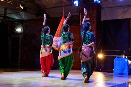 3 dancers are performing on stage in unison. they all have one leg tucked behind the other and an arm in the air