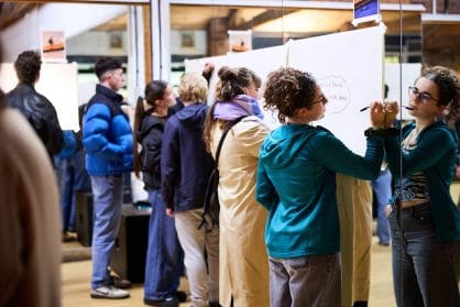 a group of people all write on big pieces of paper attached to a mirrored wall in a dance studio 
