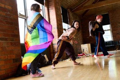 Three people move. One is draped in a pride flag