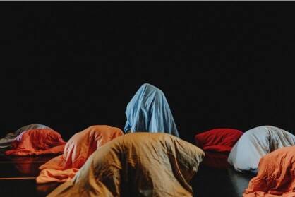 A black stage with figures draped in blankets like mountains