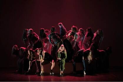 A group of performers pose in a circle in low lighting