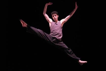 A boy performs an impressive jump with his legs outstretched on stage