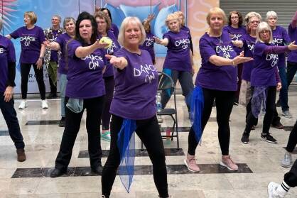 A group of women in purple Dance On T-Shirts perform in a shopping centre