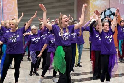 A group of women in purple Dance On T-Shirts perform in a shopping centre