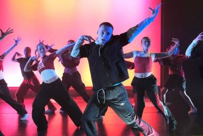 A group perform Hip-Hop on stage in black white and red costumes.