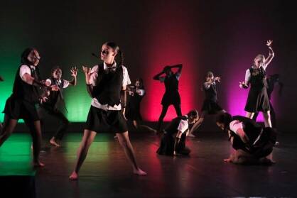 A group of dancers in black and white school uniforms perform on stage