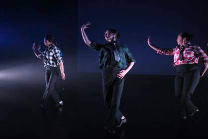 A group of performers in shirts and ties dance on stage