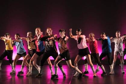 A group of young dancers in football shirts perform in a triangle formation