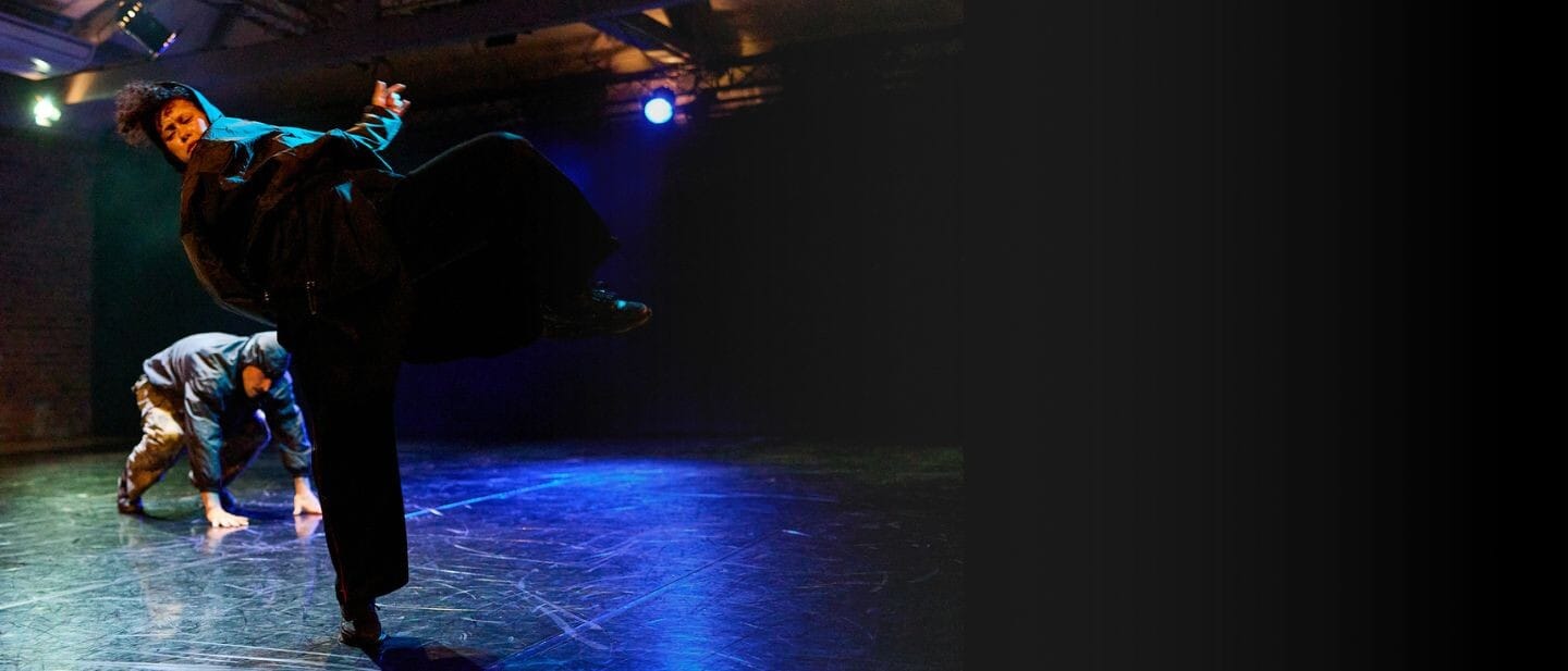 Two dancers move in against a dark background