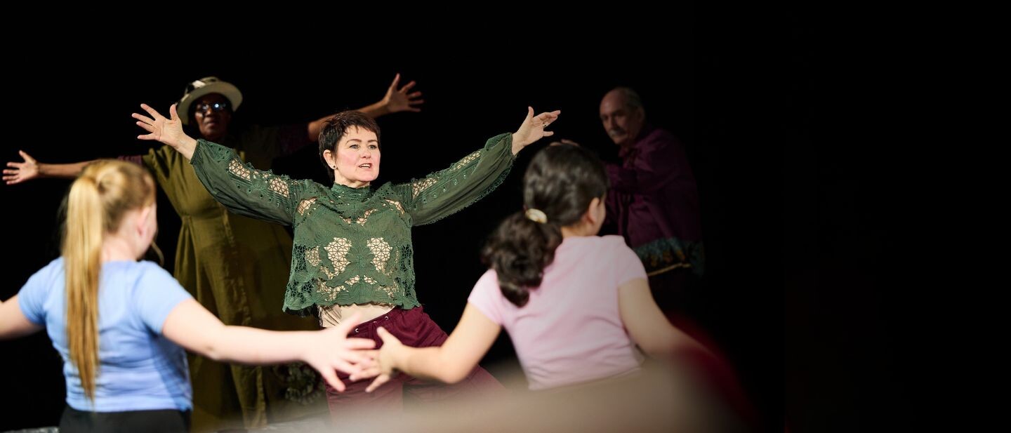 A dance artist stands with her arms out teaching a group
